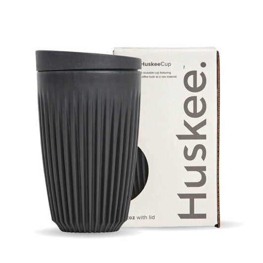 12oz Charcoal Huskee Reusable Coffee Cup with Lid in front of its packaging box